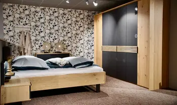 Modernes Schlafzimmer mit Holzbett, dunklem Kleiderschrank mit Holzdetails, gemusterter Tapete und abgestimmten Möbeln in natürlicher, wohnlicher Gestaltung.
